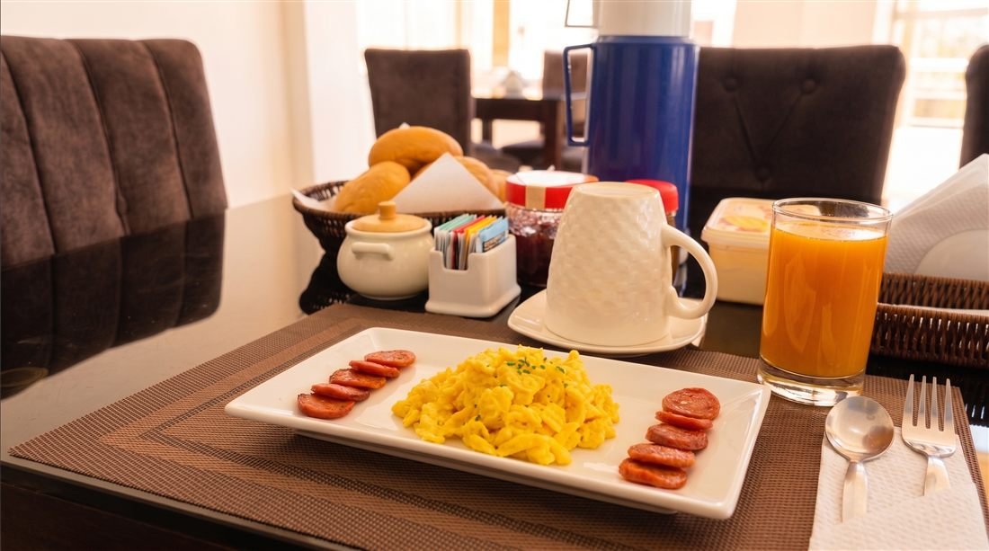Plato de desayuno americano: huevos revueltos, salchicha, pan y jugo de naranja